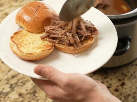 Fall-apart shredded beef chuck roast in rich brown gravy with caramelized onions in a slow cooker