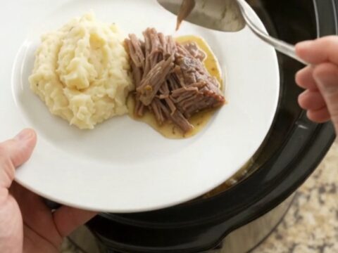 Slow cooker rosemary thyme butter chuck roast, shredded and served over mashed potatoes with golden jus.