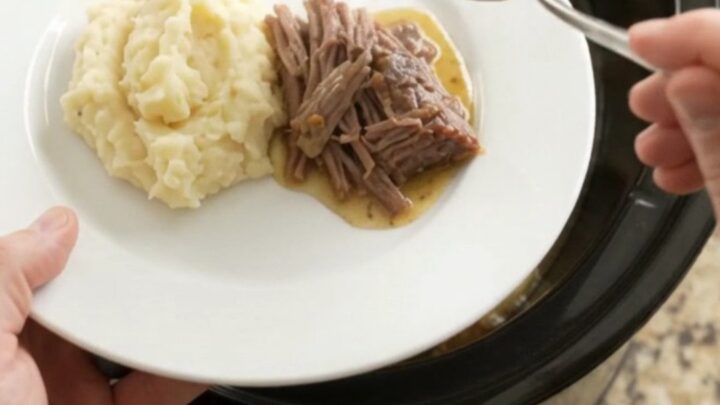 Slow cooker rosemary thyme butter chuck roast, shredded and served over mashed potatoes with golden jus.