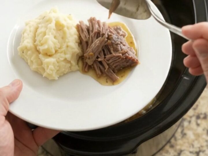 Slow cooker rosemary thyme butter chuck roast, shredded and served over mashed potatoes with golden jus.