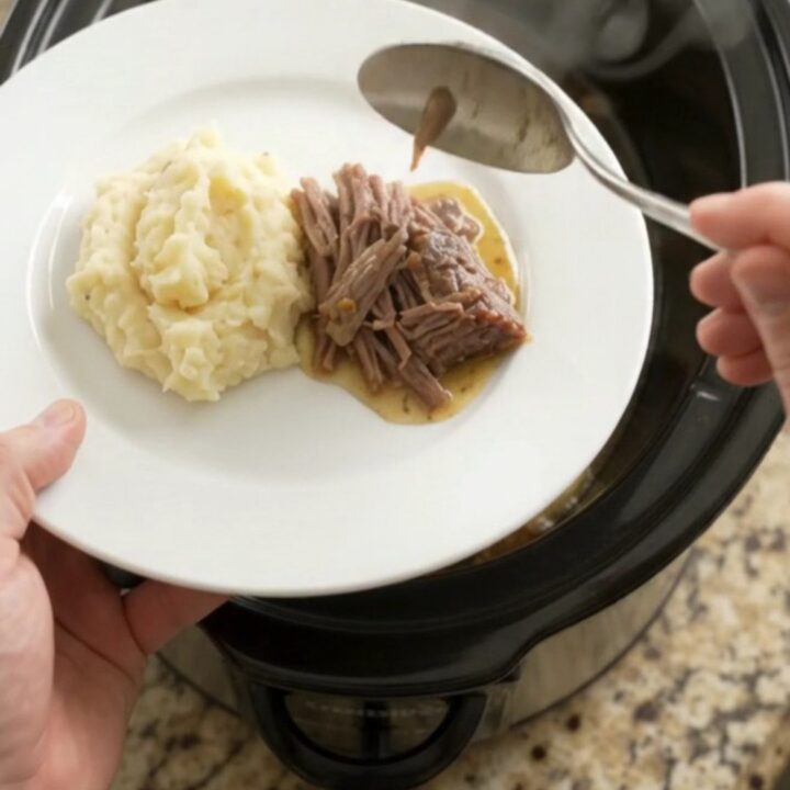 Slow cooker rosemary thyme butter chuck roast, shredded and served over mashed potatoes with golden jus.