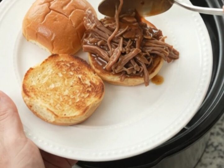 Shredded beef chuck roast in a slow cooker with gravy and herbs