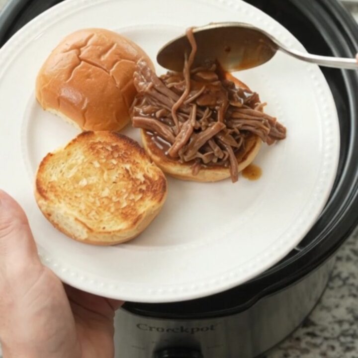Shredded beef chuck roast in a slow cooker with gravy and herbs