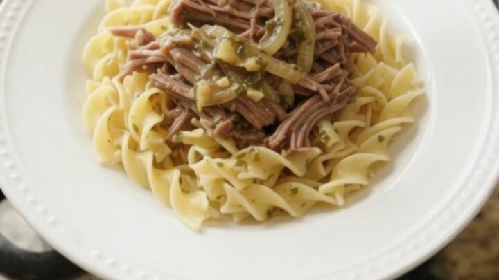 Slow-cooker French onion garlic butter chuck roast in a black Crockpot, topped with caramelized onions and herbs.