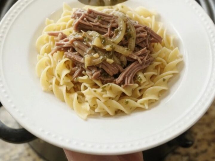 Slow-cooker French onion garlic butter chuck roast in a black Crockpot, topped with caramelized onions and herbs.