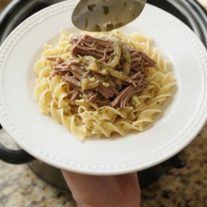 Slow-cooker French onion garlic butter chuck roast in a black Crockpot, topped with caramelized onions and herbs.