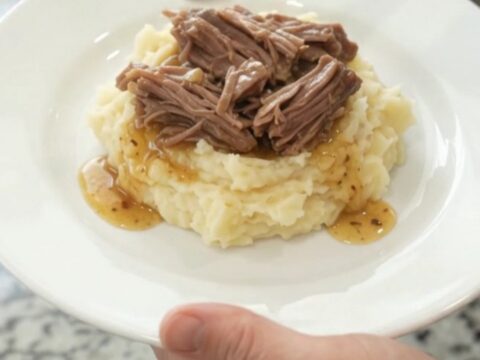 Slow-cooker chuck roast with potatoes and carrots in a black crockpot, topped with butter