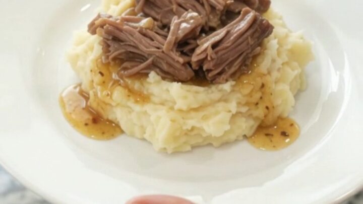 Slow-cooker chuck roast with potatoes and carrots in a black crockpot, topped with butter
