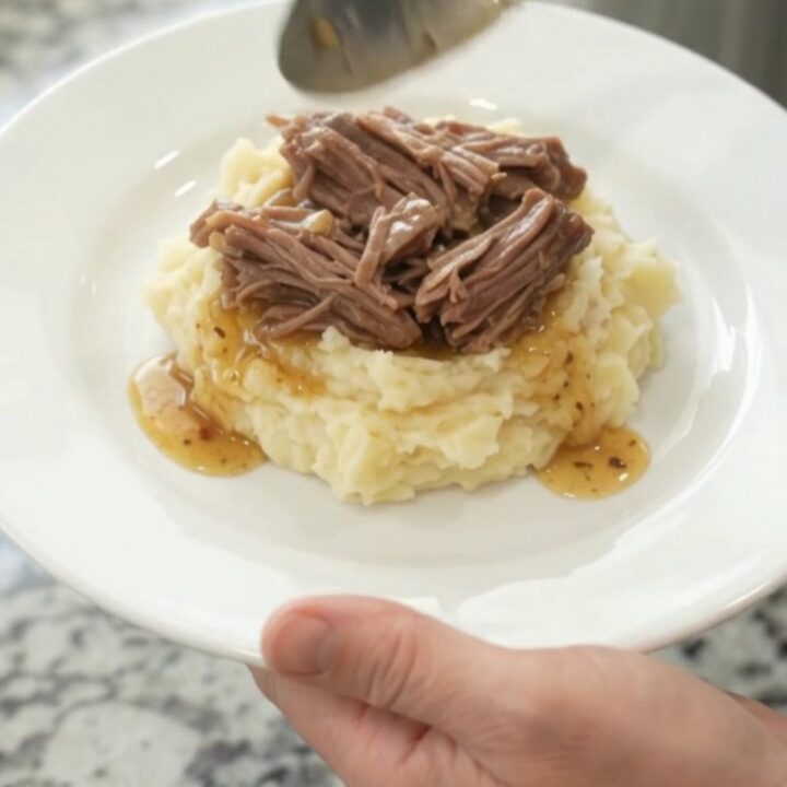 Slow-cooker chuck roast with potatoes and carrots in a black crockpot, topped with butter