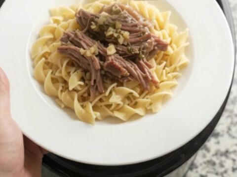 Shredded beef chuck roast with portobello mushrooms in rich gravy, served on a white plate with buttered egg noodles.