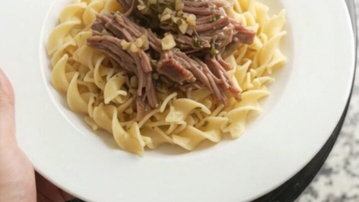 Shredded beef chuck roast with portobello mushrooms in rich gravy, served on a white plate with buttered egg noodles.
