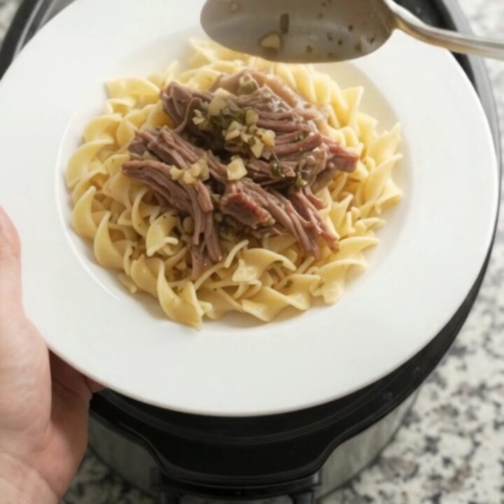 Shredded beef chuck roast with portobello mushrooms in rich gravy, served on a white plate with buttered egg noodles.