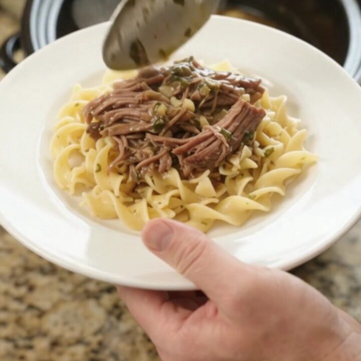 Shredded beef chuck roast with potatoes and carrots in a slow cooker, topped with butter gravy
