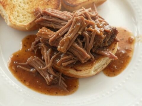 Shredded chuck roast with potatoes and carrots in a slow cooker, glistening with brown gravy.