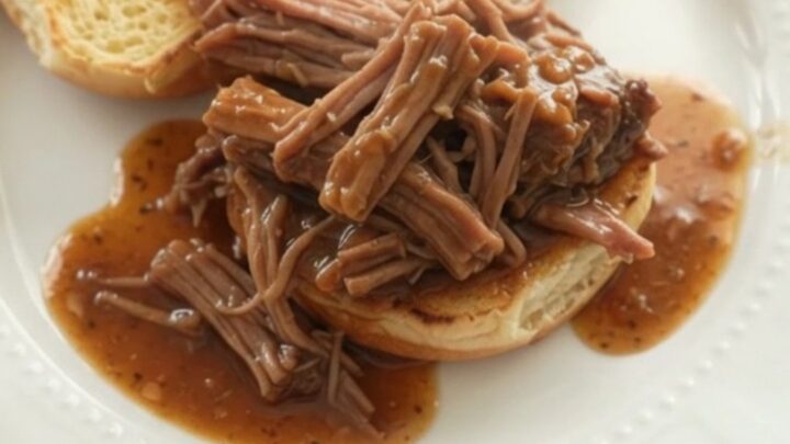 Shredded chuck roast with potatoes and carrots in a slow cooker, glistening with brown gravy.