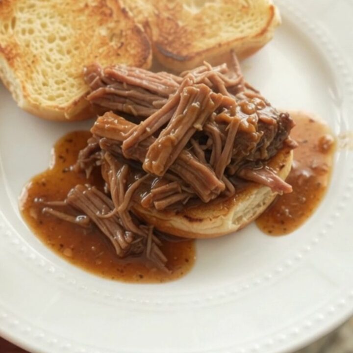 Shredded chuck roast with potatoes and carrots in a slow cooker, glistening with brown gravy.