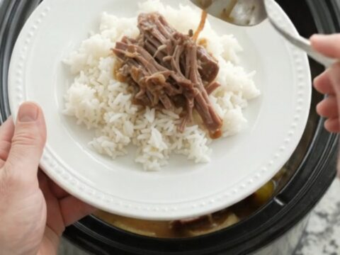 Slow cooker chuck roast with sweet peppers and creamy Dijon sauce, shredded and served on a white plate.