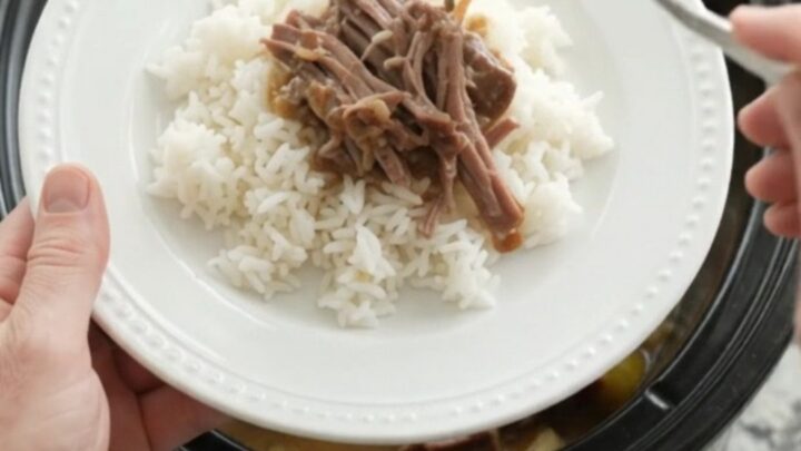 Slow cooker chuck roast with sweet peppers and creamy Dijon sauce, shredded and served on a white plate.