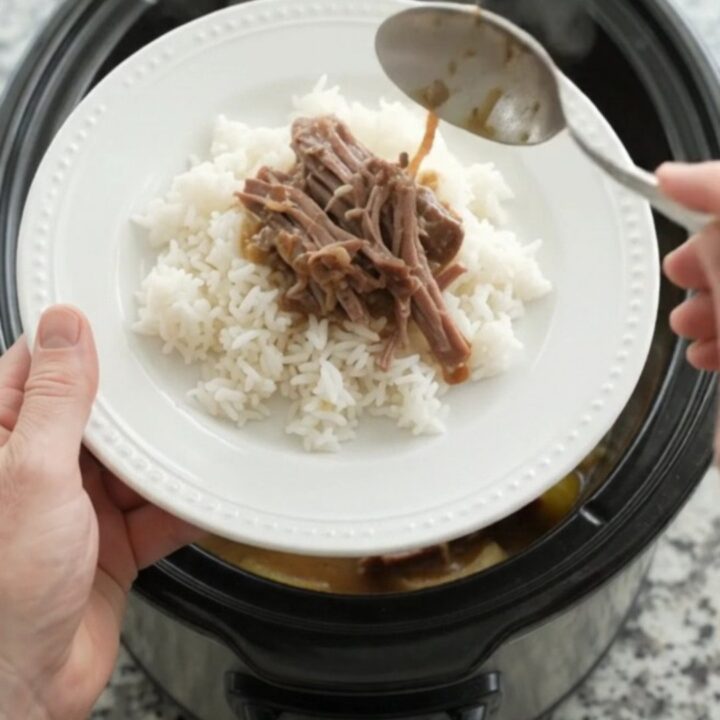 Slow cooker chuck roast with sweet peppers and creamy Dijon sauce, shredded and served on a white plate.