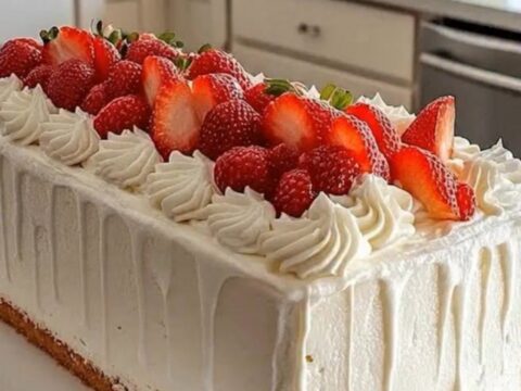A pristine rectangular loaf cake frosted in white drip glaze, topped with piped swirls and fresh strawberry halves on a white