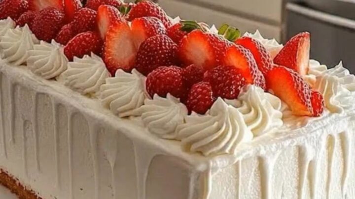 A pristine rectangular loaf cake frosted in white drip glaze, topped with piped swirls and fresh strawberry halves on a white