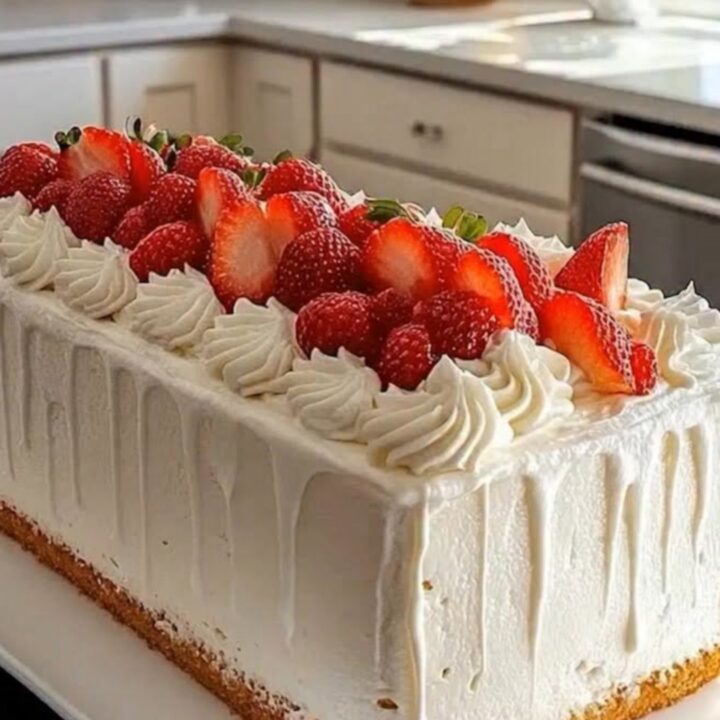 A pristine rectangular loaf cake frosted in white drip glaze, topped with piped swirls and fresh strawberry halves on a white