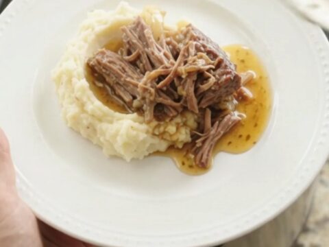 Shredded beef chuck roast with sweet peppers and onions in a slow cooker, bathed in golden butter jus.