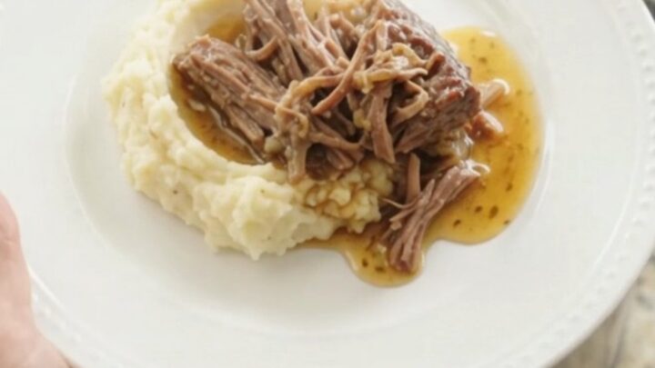 Shredded beef chuck roast with sweet peppers and onions in a slow cooker, bathed in golden butter jus.