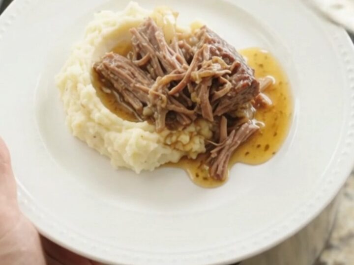 Shredded beef chuck roast with sweet peppers and onions in a slow cooker, bathed in golden butter jus.