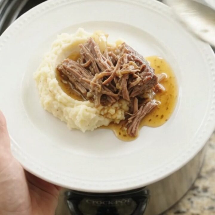 Shredded beef chuck roast with sweet peppers and onions in a slow cooker, bathed in golden butter jus.