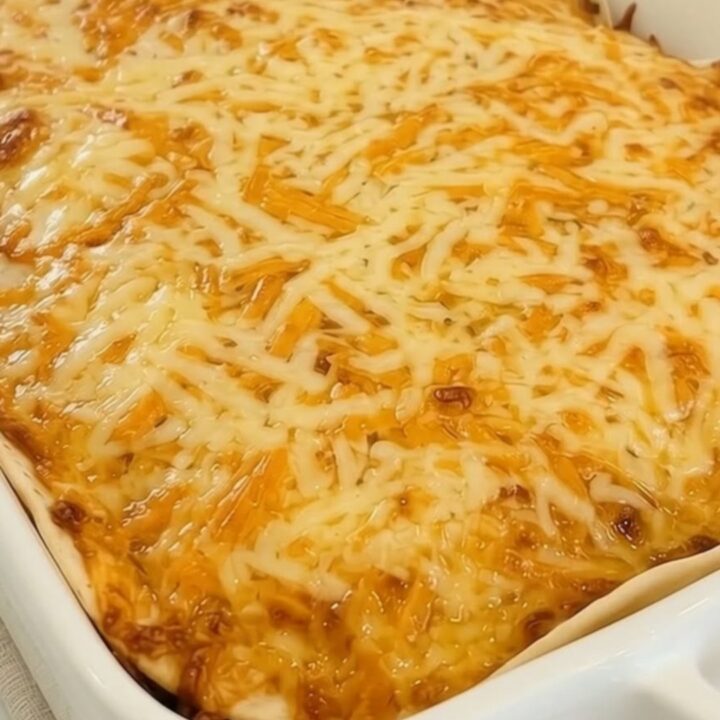 A slice of cheesy taco lasagna casserole being lifted from a white ceramic dish with a massive cheese pull.