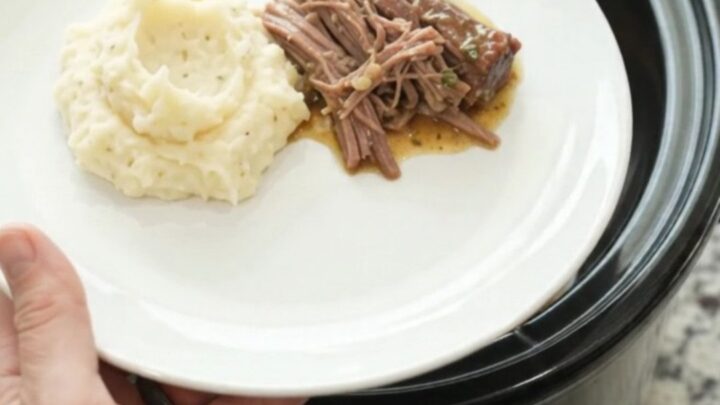 Shredded beef brisket in a slow cooker with buttery gravy, being lifted with a spoon