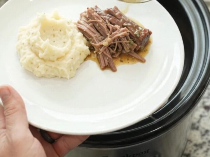Shredded beef brisket in a slow cooker with buttery gravy, being lifted with a spoon