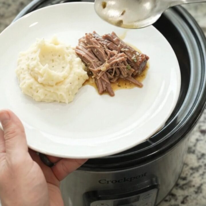 Shredded beef brisket in a slow cooker with buttery gravy, being lifted with a spoon