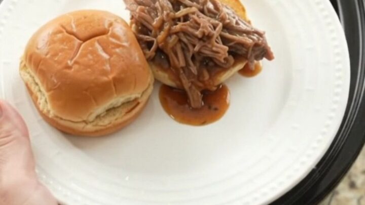 Shredded beef brisket in a slow cooker with rich brown gravy, topped with butter.