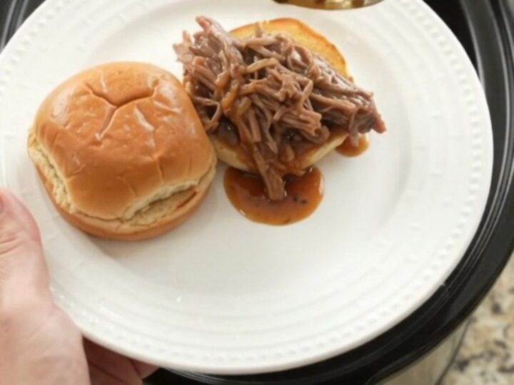 Shredded beef brisket in a slow cooker with rich brown gravy, topped with butter.