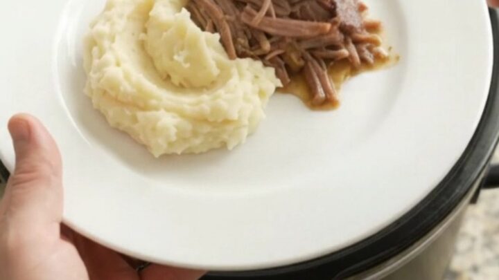 Fork-shredded beef brisket in a slow cooker with pearl onions and buttery jus.