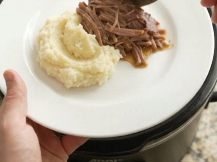 Fork-shredded beef brisket in a slow cooker with pearl onions and buttery jus.