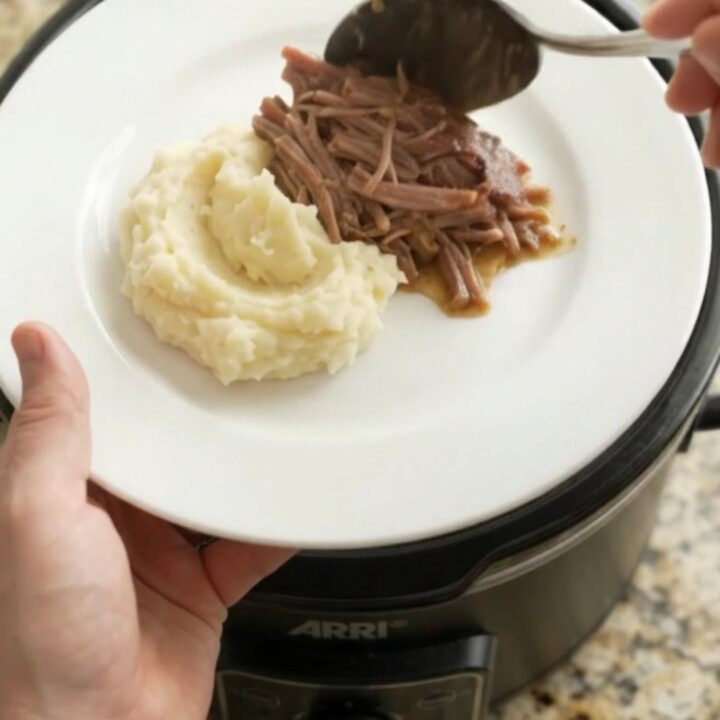 Fork-shredded beef brisket in a slow cooker with pearl onions and buttery jus.