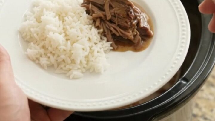 Shredded beef brisket with creamy Dijon gravy in a slow cooker, garnished with pearl onions
