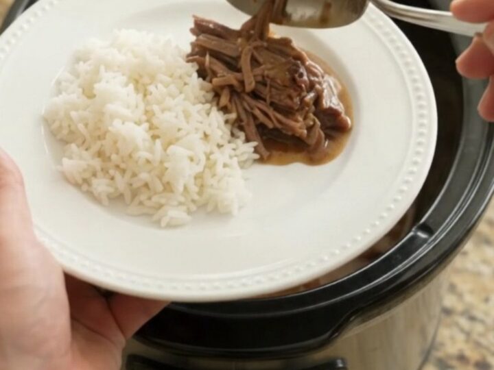 Shredded beef brisket with creamy Dijon gravy in a slow cooker, garnished with pearl onions