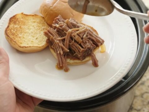 Shredded beef brisket with caramelized onions in a slow cooker, topped with gravy