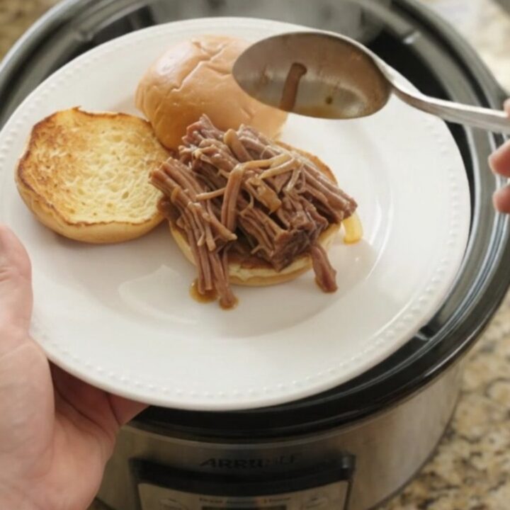 Shredded beef brisket with caramelized onions in a slow cooker, topped with gravy