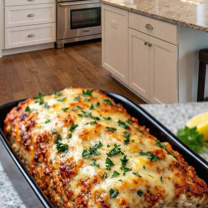 A whole baked garlic parmesan chicken meatloaf in a black pan on a granite surface.