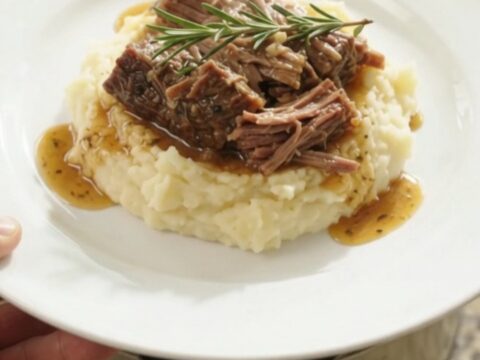 Fork-shredded beef brisket in a slow cooker with garlic and herbs in golden butter jus.