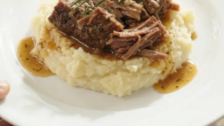 Fork-shredded beef brisket in a slow cooker with garlic and herbs in golden butter jus.