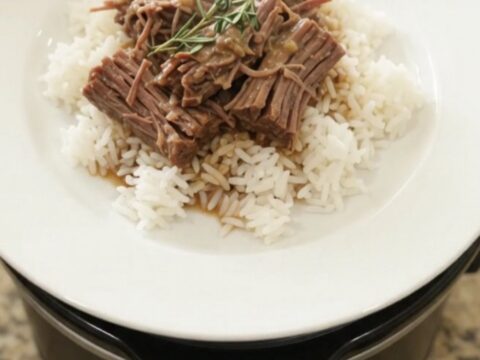Slow-cooker Dijon cream beef brisket in a black crockpot, topped with herbs and creamy gravy