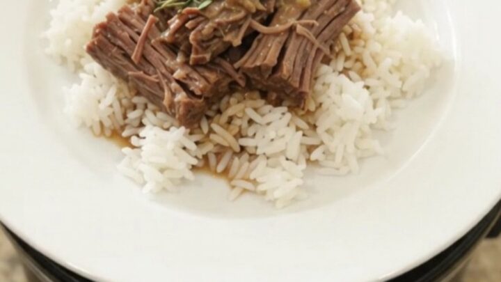 Slow-cooker Dijon cream beef brisket in a black crockpot, topped with herbs and creamy gravy