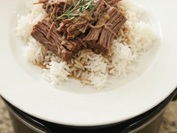 Slow-cooker Dijon cream beef brisket in a black crockpot, topped with herbs and creamy gravy