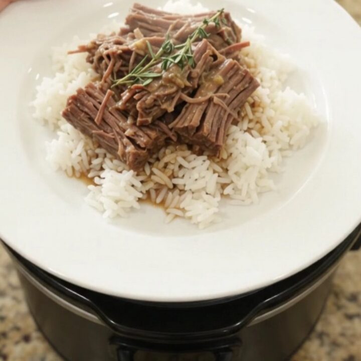 Slow-cooker Dijon cream beef brisket in a black crockpot, topped with herbs and creamy gravy